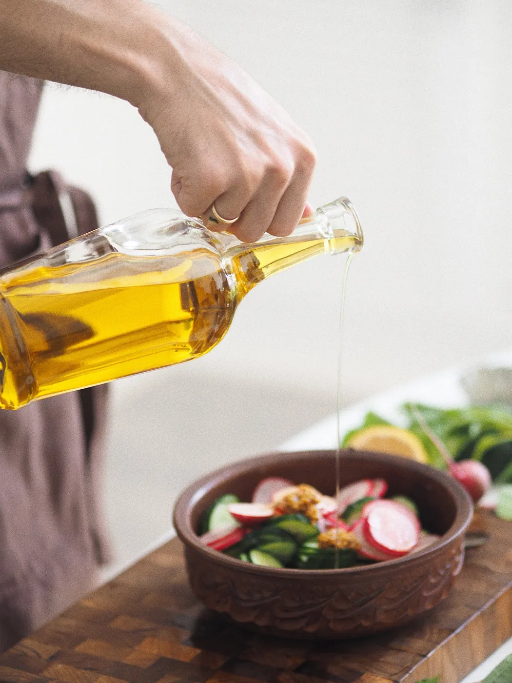 Olive oil being poured over a salad of radish and cucumber.